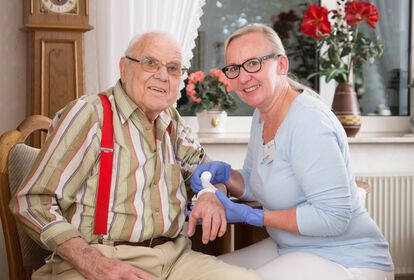 Älterer Mann bekommt einen Verband am Unterarm von weiblicher Pflegekraft.