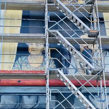 Zwei Männer stehen auf einem Baugerüst und restaurieren ein Wandbild