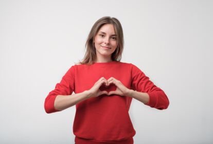 junge Frau mit rotem Pulli formt mit ihren Händen ein Herz vor der Brust
