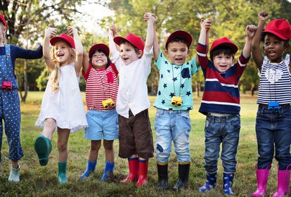 Kinder mit roten Cappies auf, stehen in einer Reihe, lachen in die Kamera, halten sich gegenseitig an den hochgehobenen Händen.