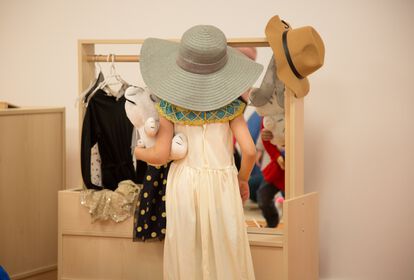 Von hinten fotografiert: Kind trägt großen Hut und im Arme ein Kuscheltier. Es steht vor einem Verkleidungsschrank