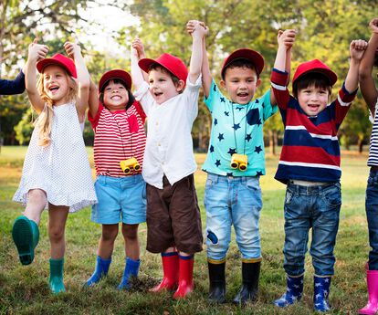 Kinder mit roten Cappies auf, stehen in einer Reihe, lachen in die Kamera, halten sich gegenseitig an den hochgehobenen Händen.