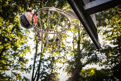 Basketball in der Luft am Rand eines Basketballkorbs. Im Hintergrund Baumkronen