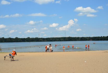 Kinder in Schwimmwesten spielen am Sandstrand und im Wasser des Unisees.