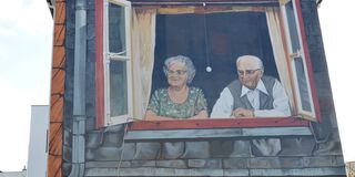 Das sanierte Wandbild erstrahlt in neuem Glanz. Darauf zu sehen sind eine ältere Frau und ein älterer Herr, die gemeinsam aus dem Fenster schauen