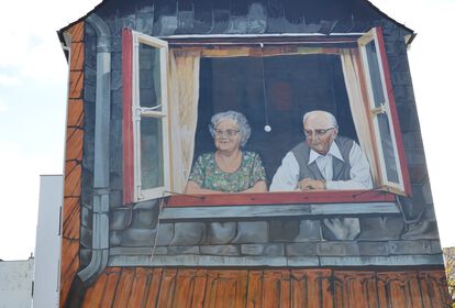 Das sanierte Wandbild erstrahlt in neuem Glanz. Darauf zu sehen sind eine ältere Frau und ein älterer Herr, die gemeinsam aus dem Fenster schauen